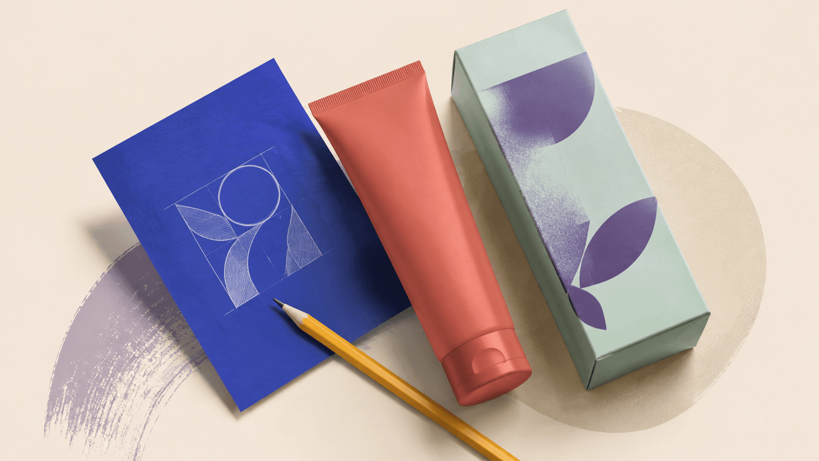 Brand collateral on cream: a navy brochure carrying a logo mark, a coral tube and a mint carton, with a pencil and a swipe of purple paint